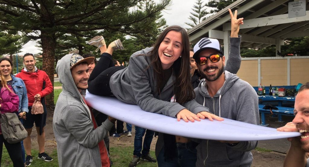 chica subida en una tabla de surf y los amigos la suben